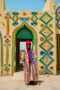 A man in traditional clothing stands in front of a colorful building