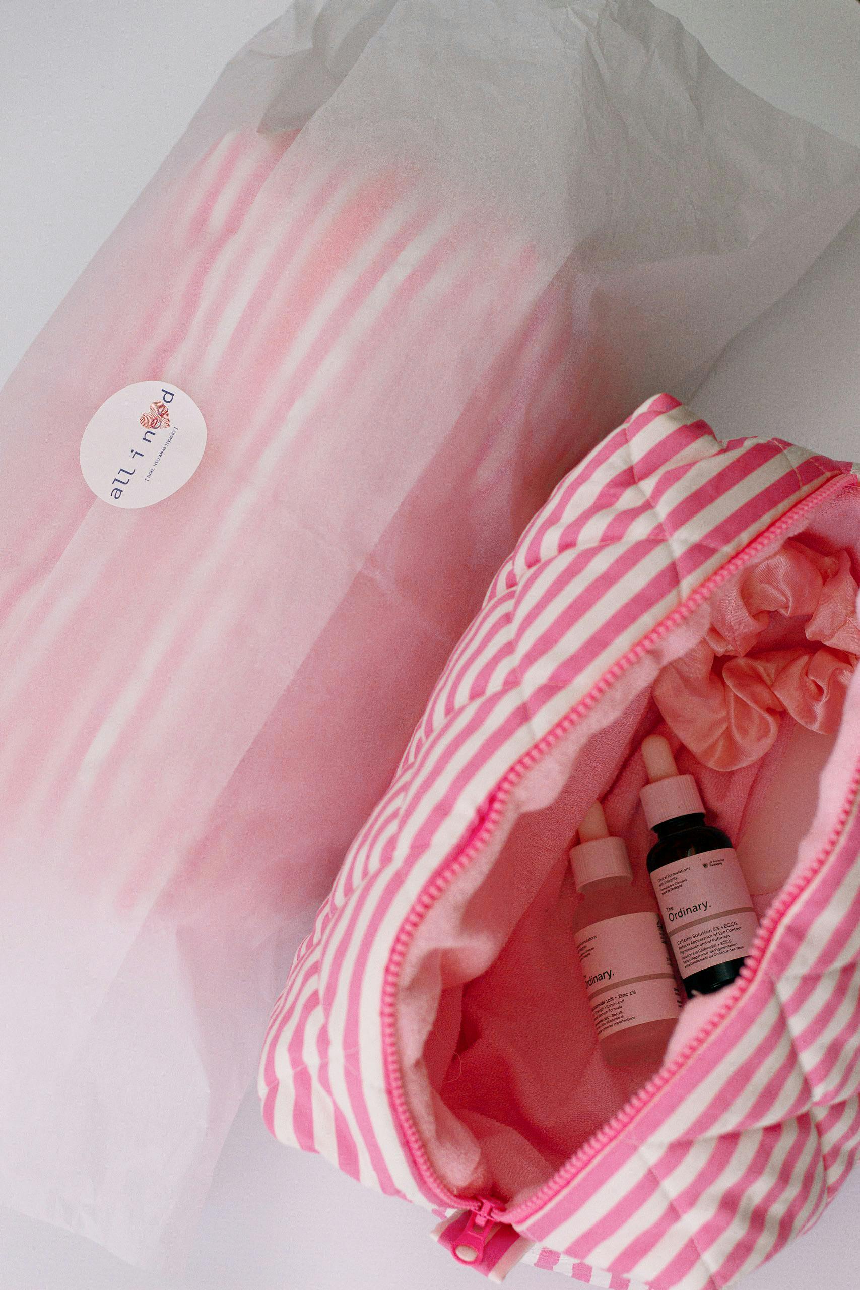 A top view of a pink striped cosmetic bag containing skincare products, showcasing beauty essentials.