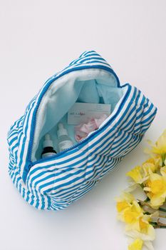 Open blue striped makeup bag with skincare items and daffodils. Ideal for beauty and travel.