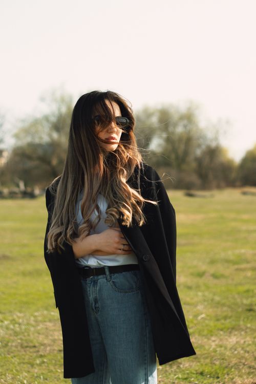 Free Young fashionable woman with long hair in sunglasses standing in a sunny park. Stock Photo
