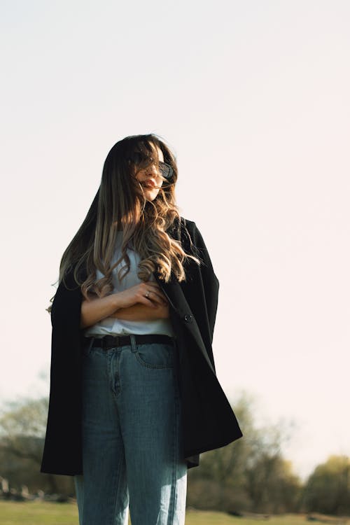 A woman in jeans and a black coat standing in a field