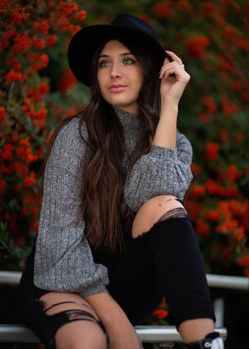 Young Woman in a Sweater, Ripped Jeans and a Hat Sitting Outside 