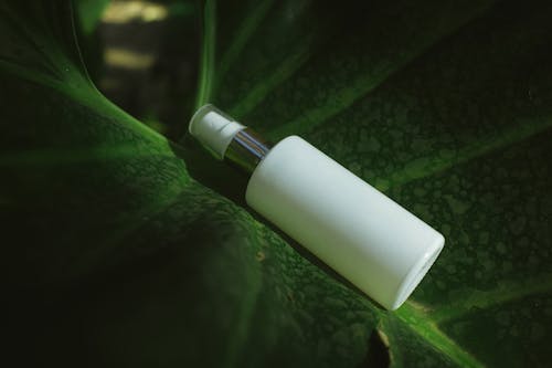 A white bottle sitting on top of a green leaf