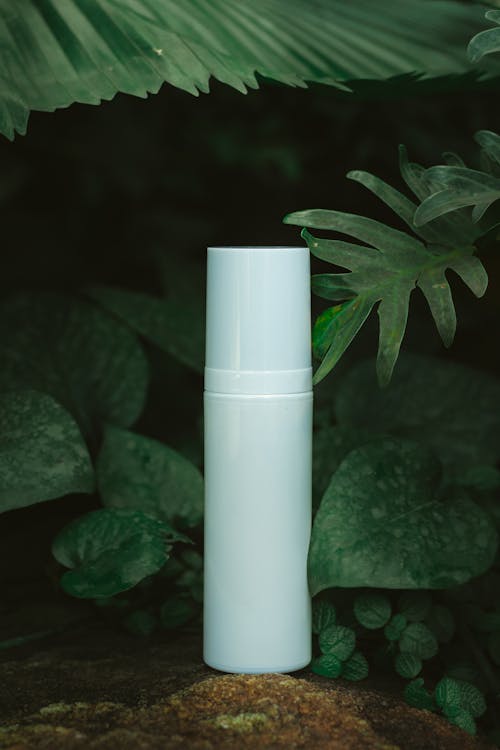 A white bottle sitting on top of some leaves