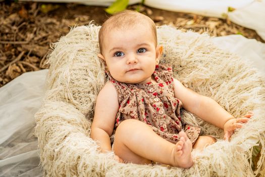 Cute baby girl sitting in a fluffy basket, enjoying the outdoors.