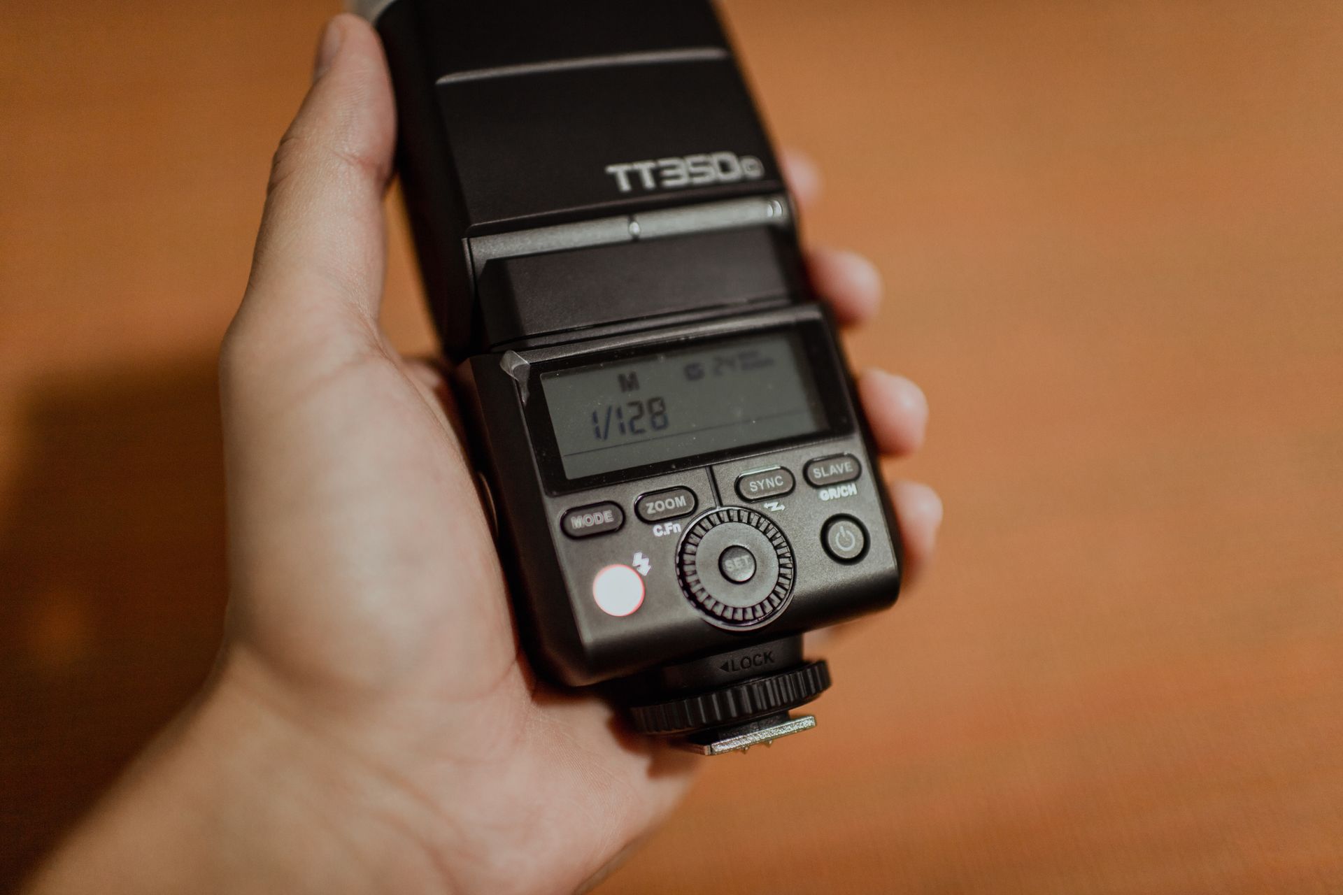 A close-up of a hand holding a modern camera flash device indoors.