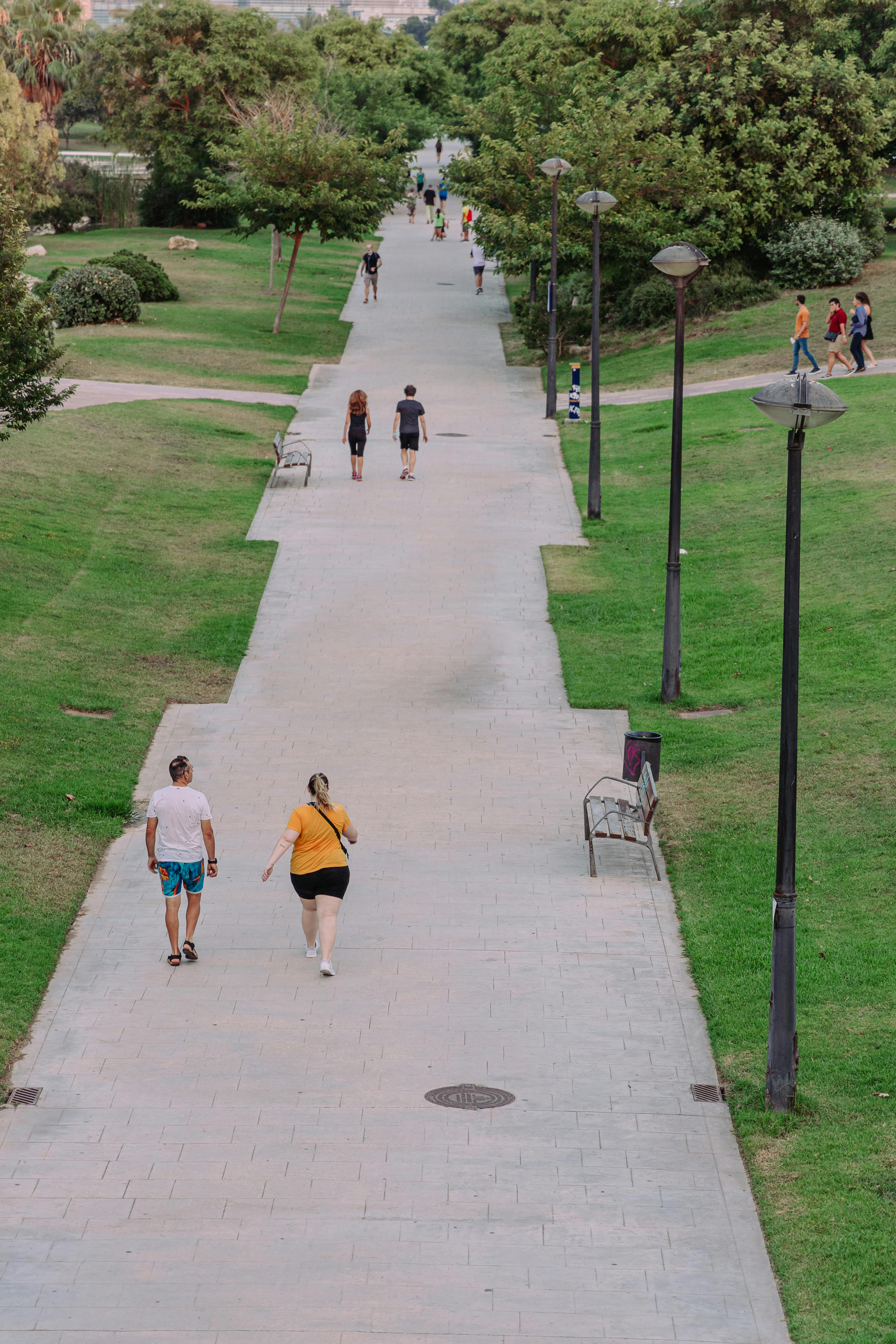 two people walking down a sidewalk in a park