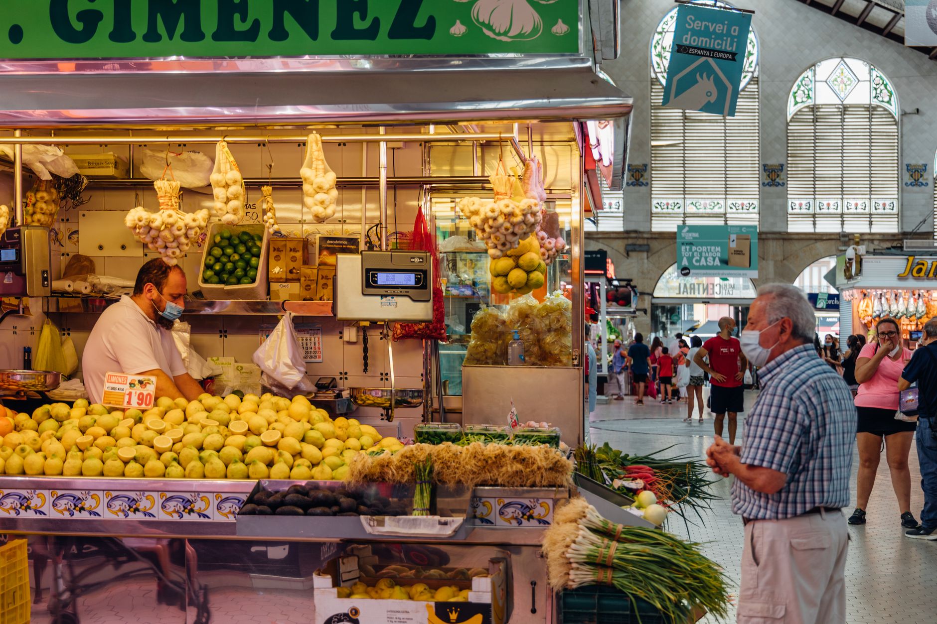 A bustling market stall in Valencia, Spain with fresh produce and people shopping.