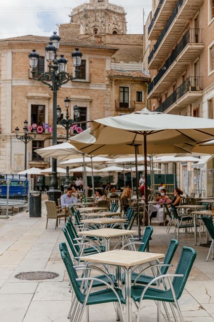 Lively outdoor cafe in Valencia's historic square with tables and umbrellas under a summer sky.