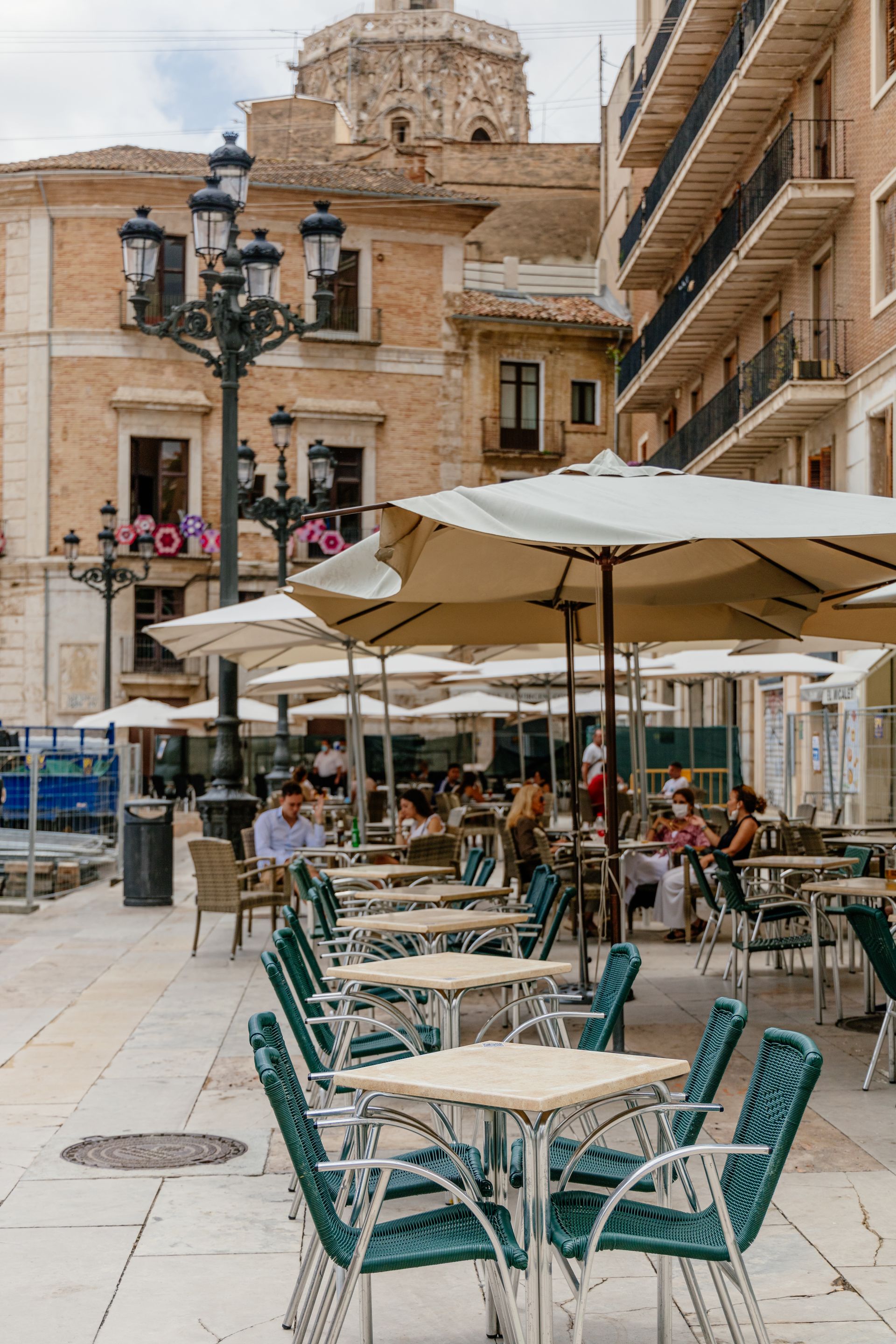 Lively outdoor cafe in Valencia's historic square with tables and umbrellas under a summer sky.