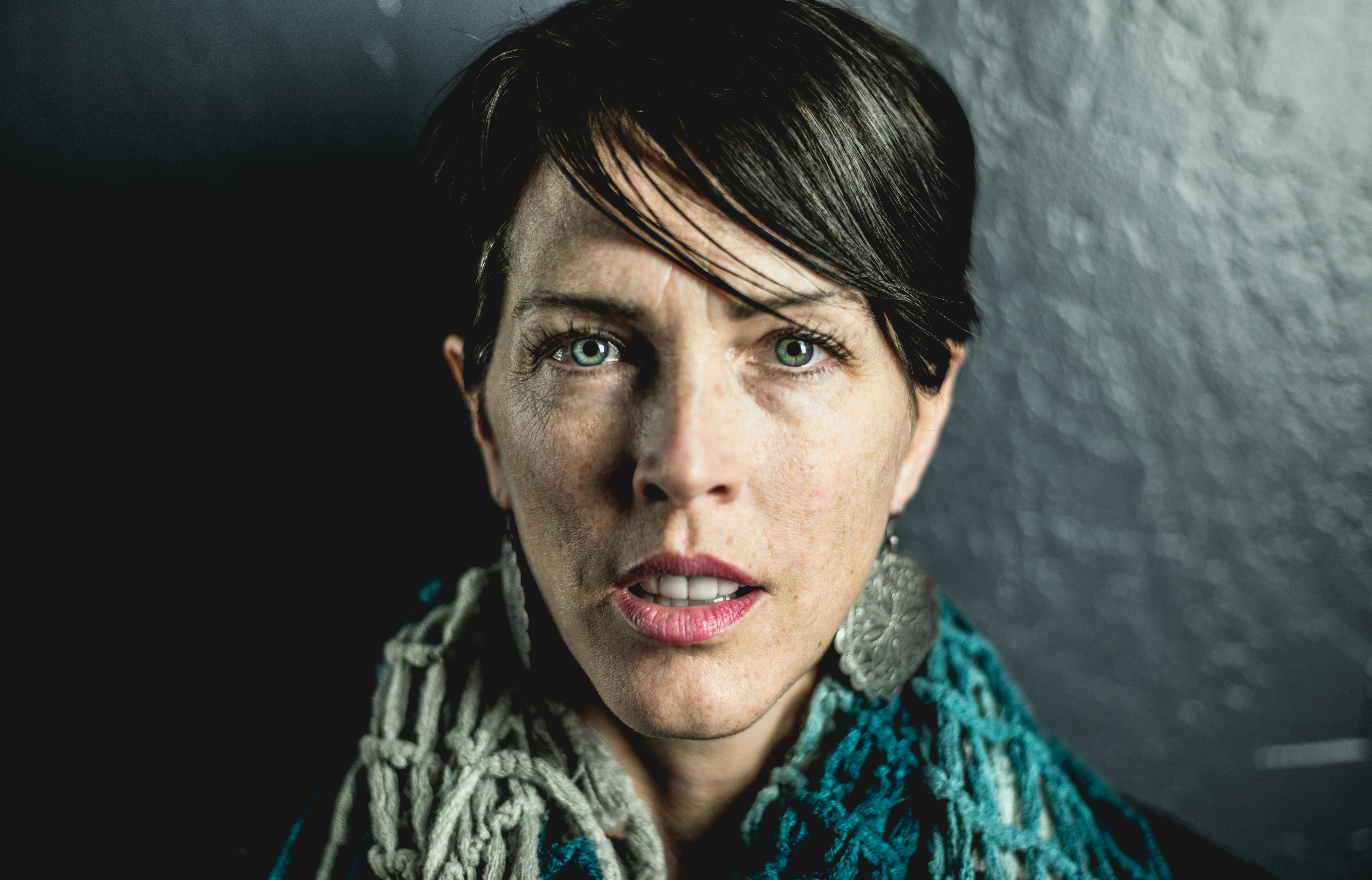 Close-up portrait of a woman with an intense expression, wearing a warm scarf and earrings, against a dark background.