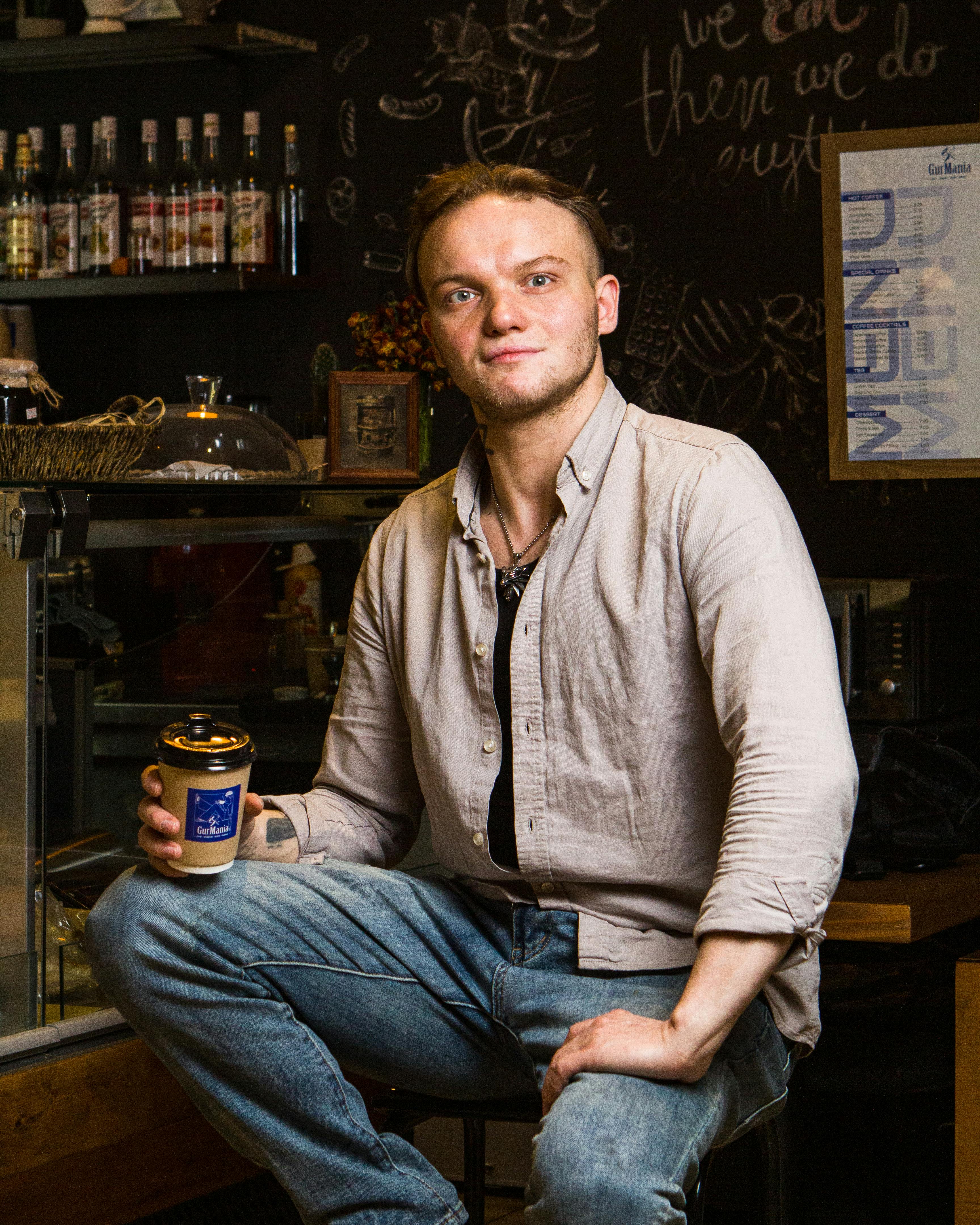 Man sitting in a café holding a coffee cup, wearing casual attire.