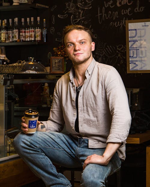 A man sitting in front of a coffee shop holding a cup