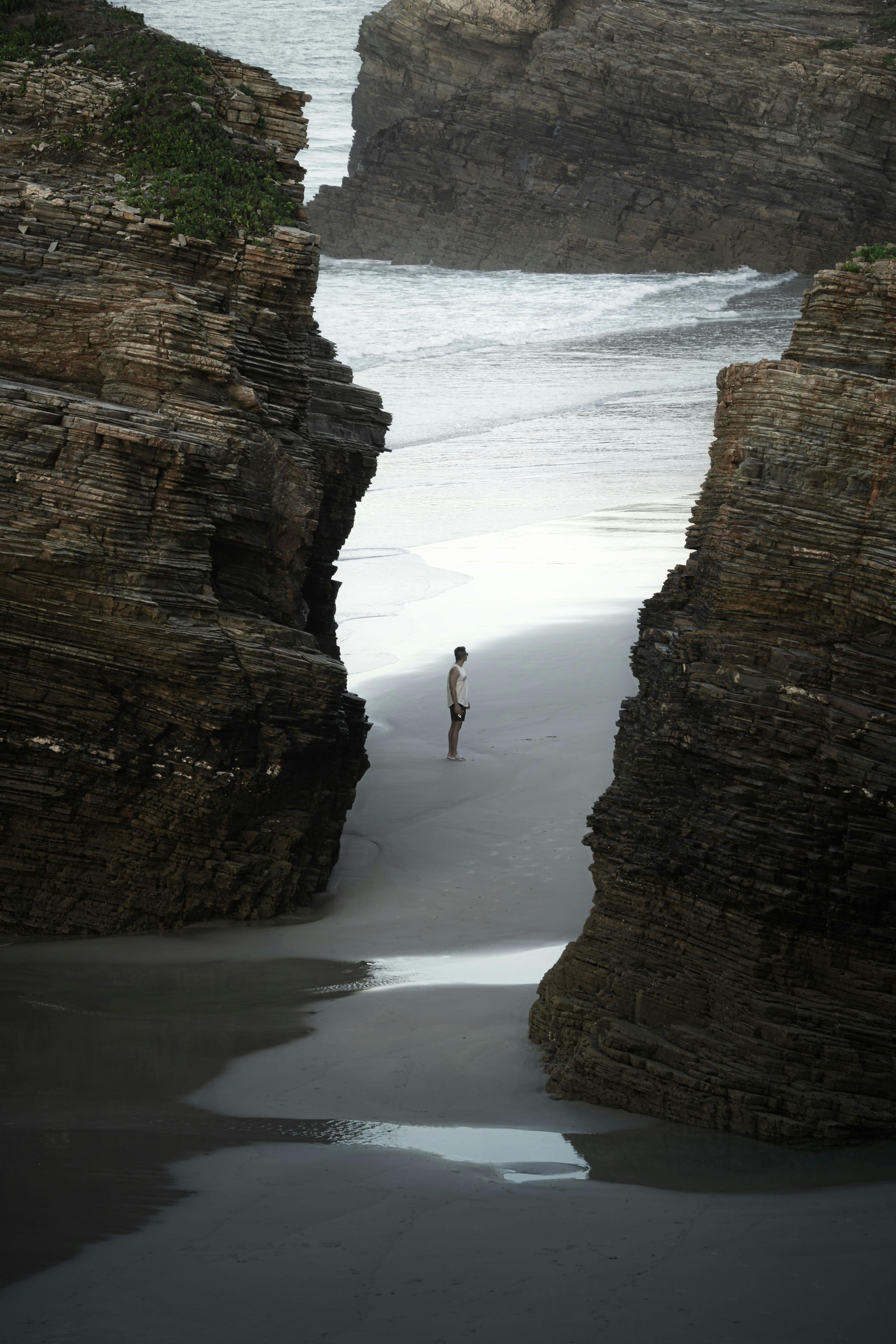 A lone traveler stands between towering cliffs at As Catedrais Beach in Ribadeo, Spain, capturing the essence of solitude and nature.