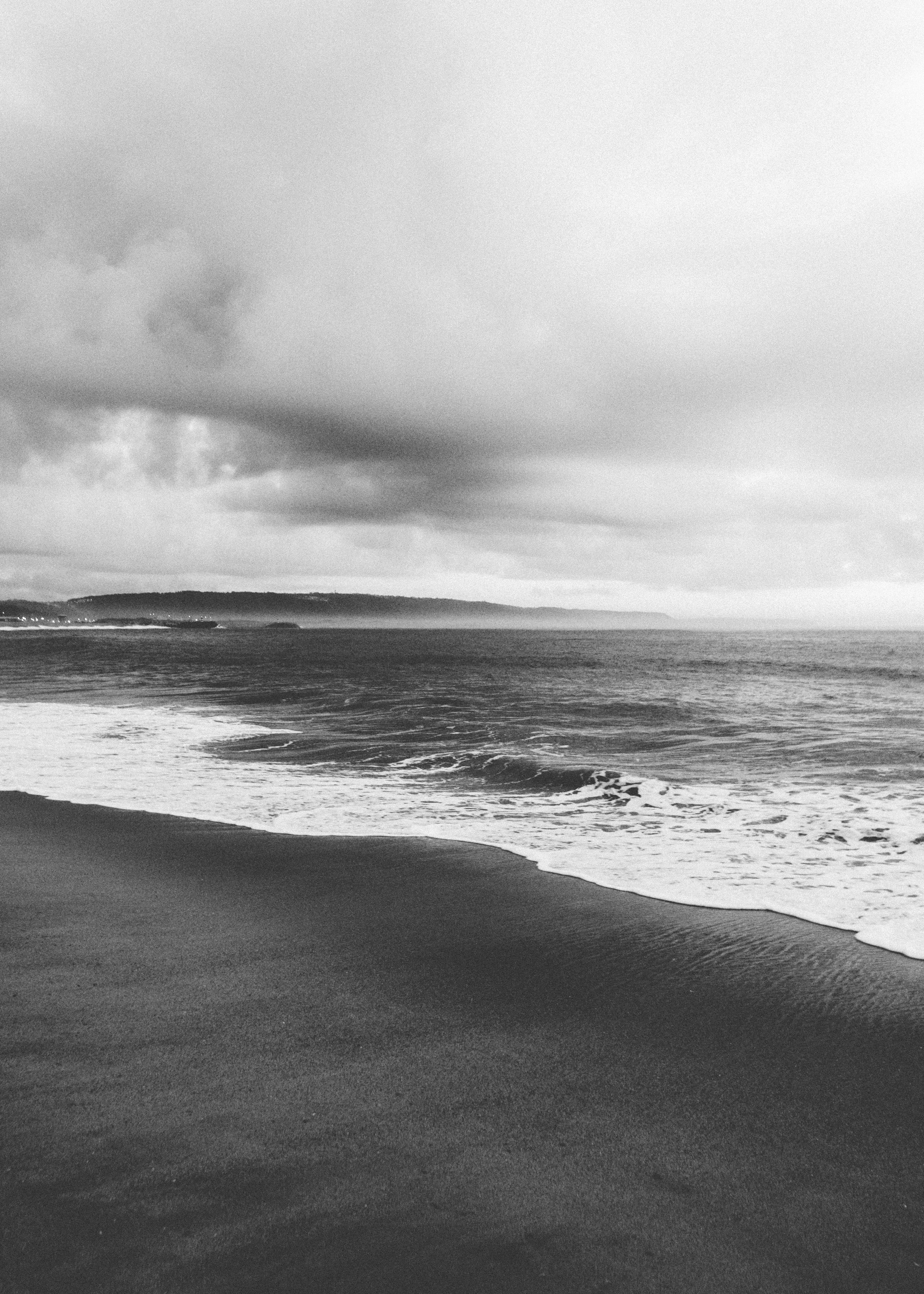 A tranquil black and white coastal scene featuring gentle waves and dramatic clouds.