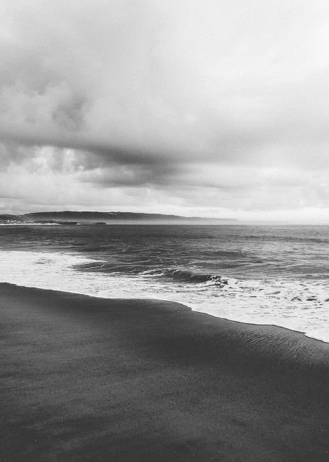 A tranquil black and white coastal scene featuring gentle waves and dramatic clouds.