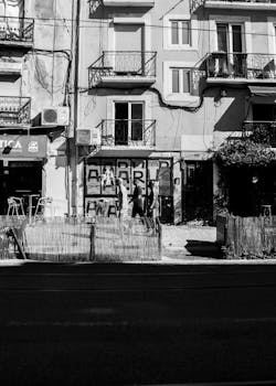 Vertical black and white photo of an urban street with residential buildings and pedestrians.