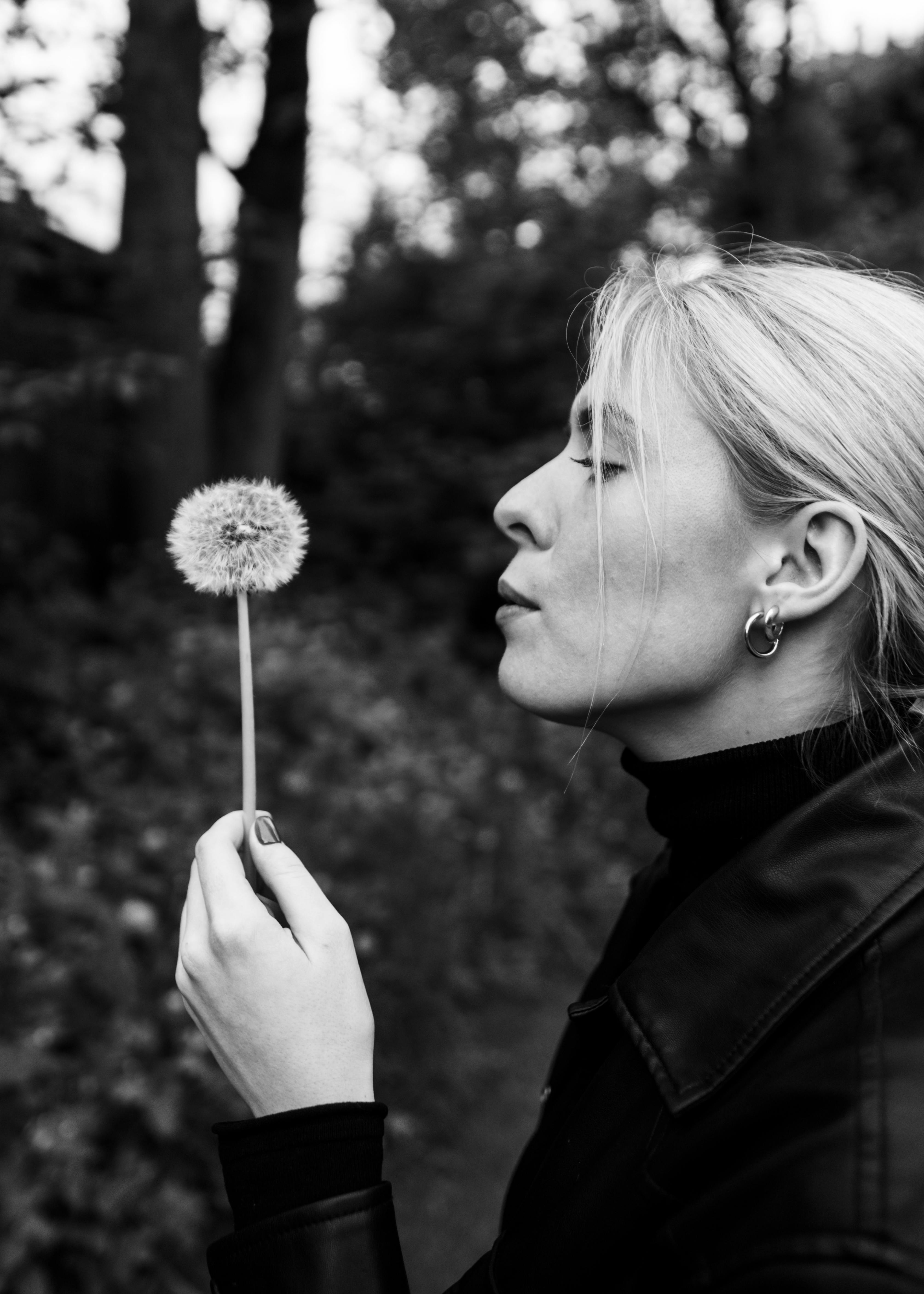 Elegant black and white portrait of a woman blowing a dandelion, capturing a serene moment in nature.
