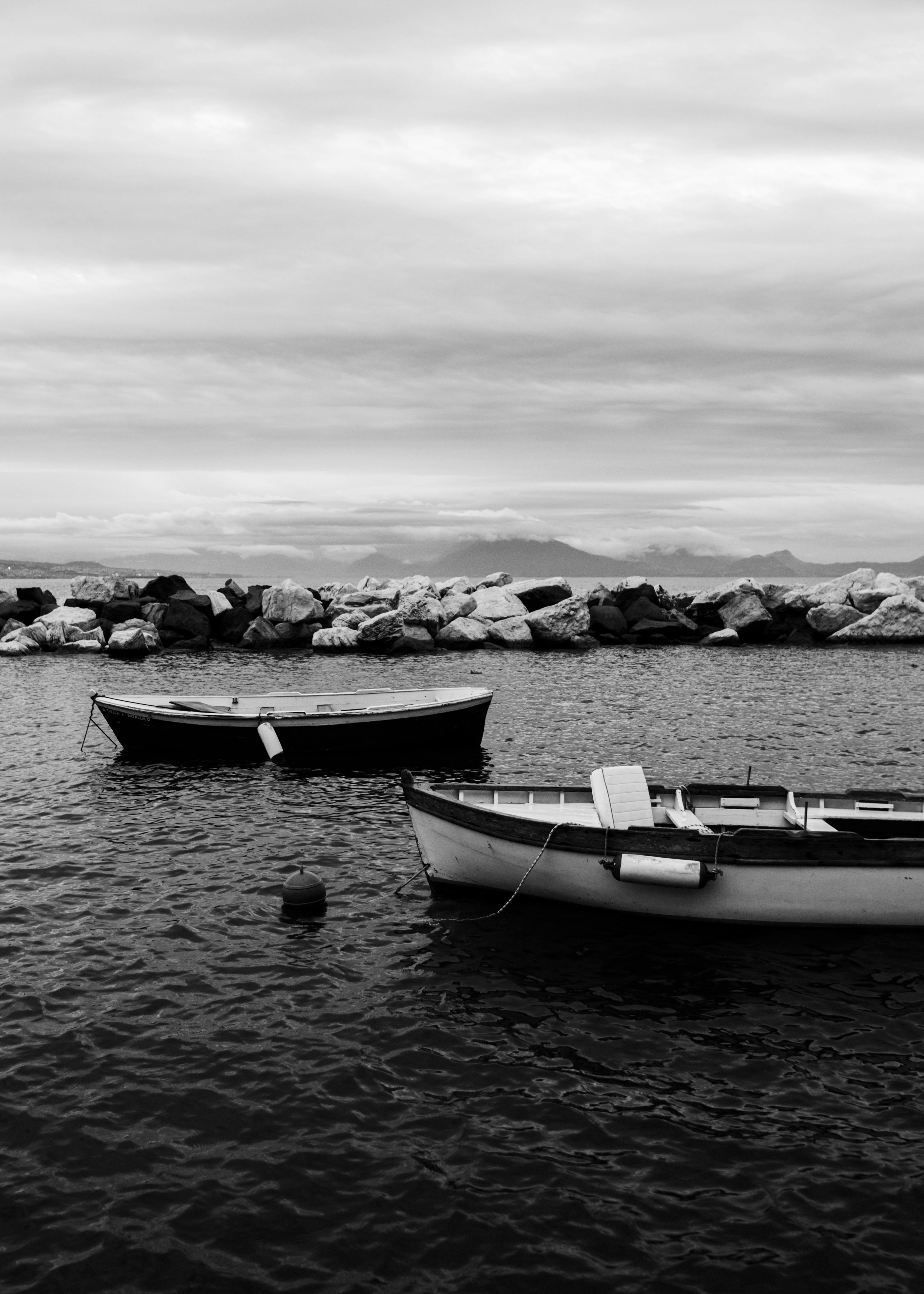 Calm seascape with two boats on a rocky shore in monochrome.
