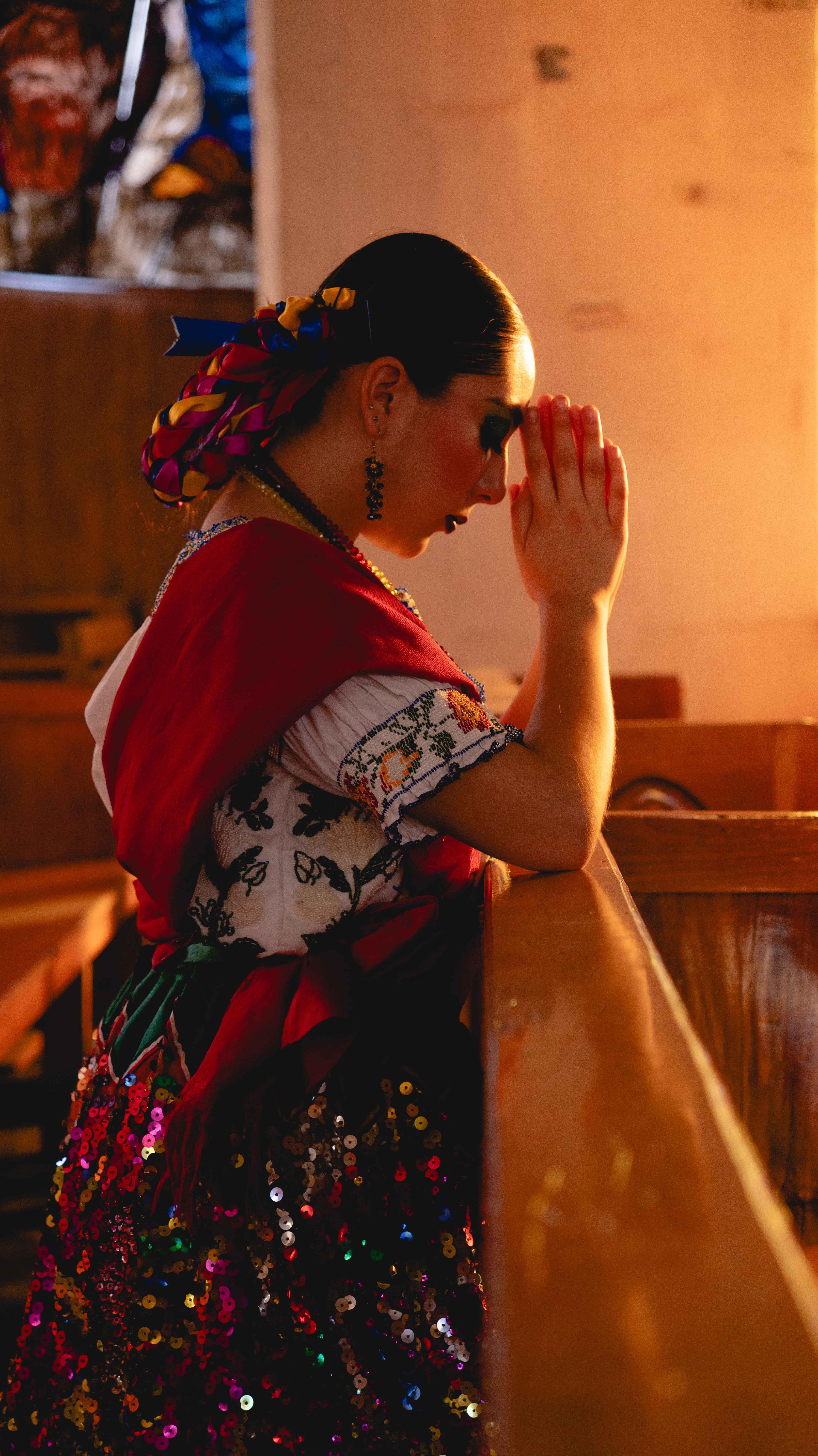 A woman in colorful Mexican dress prays in a sunlit church in Huauchinango, Mexico.