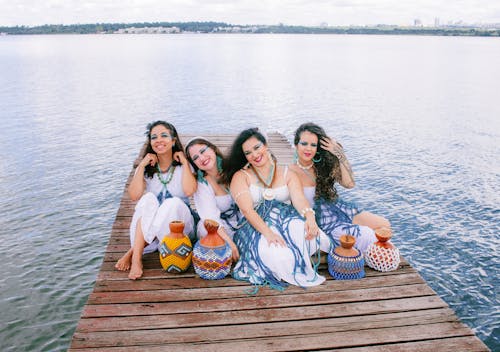 Free Three women sitting on a dock with a lake in the background Stock Photo