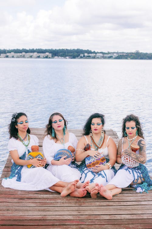 Free Four women sitting on a dock with a lake in the background Stock Photo