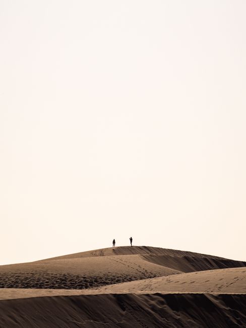 Two people silhouetted on sand dunes in Las Palmas, creating a striking minimalist view.