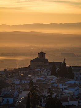 An atmospheric view of Granada, Spain, under a misty sunset sky, showcasing silhouette and urban charm.