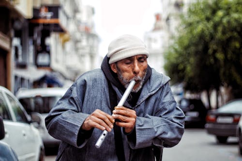 Elderly Man Playing a Flute on a Street in City 