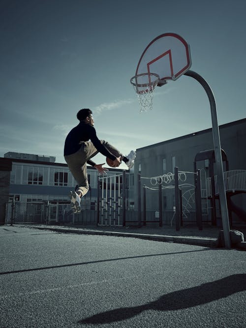 A skateboarder is jumping over a basketball hoop