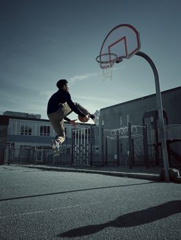 Athletic young man jumping to score a basketball hoop on an outdoor court.