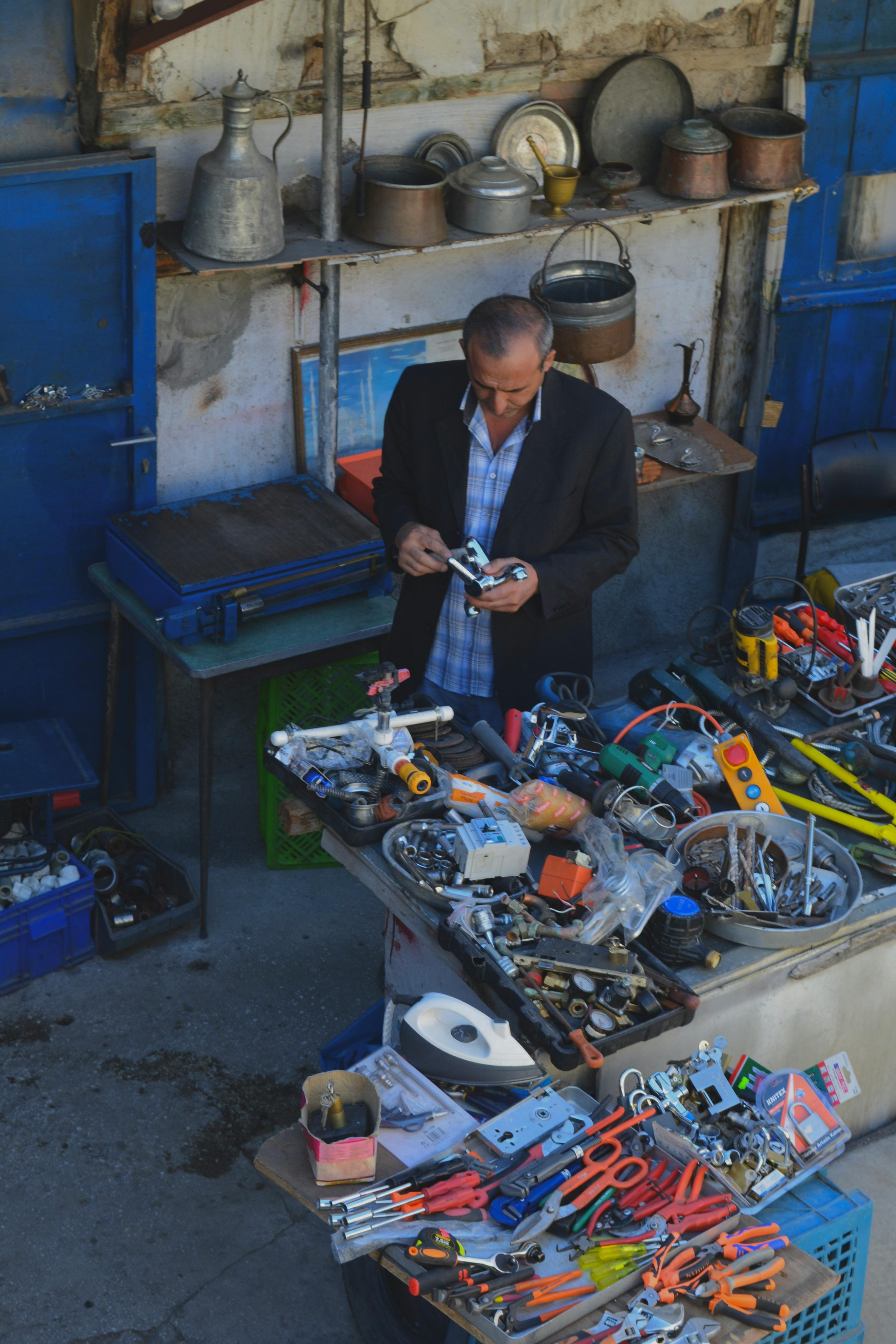 Senior vendor arranging tools in a bustling outdoor market stall.