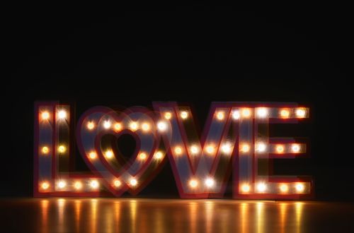 Free A close-up of an illuminated 'LOVE' sign with warm glowing lights against a dark background. Stock Photo