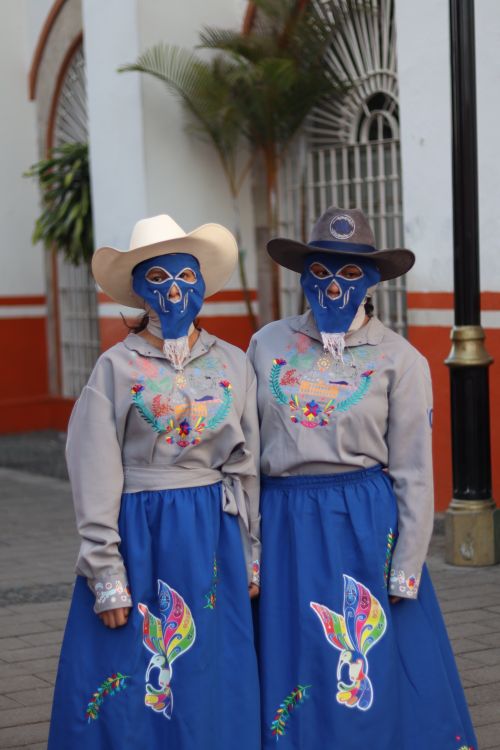 Free Two women in vibrant, traditional Mexican outfits with masks and hats in a street setting. Stock Photo