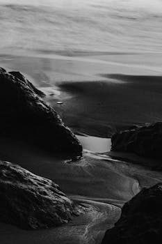 Moody black and white photo of a rocky shoreline with waves gently lapping at the shore.