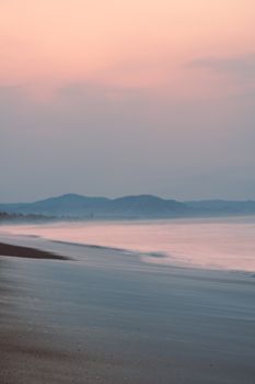 A calm beach scene at sunset with soft waves lapping on the shore under a pastel sky.