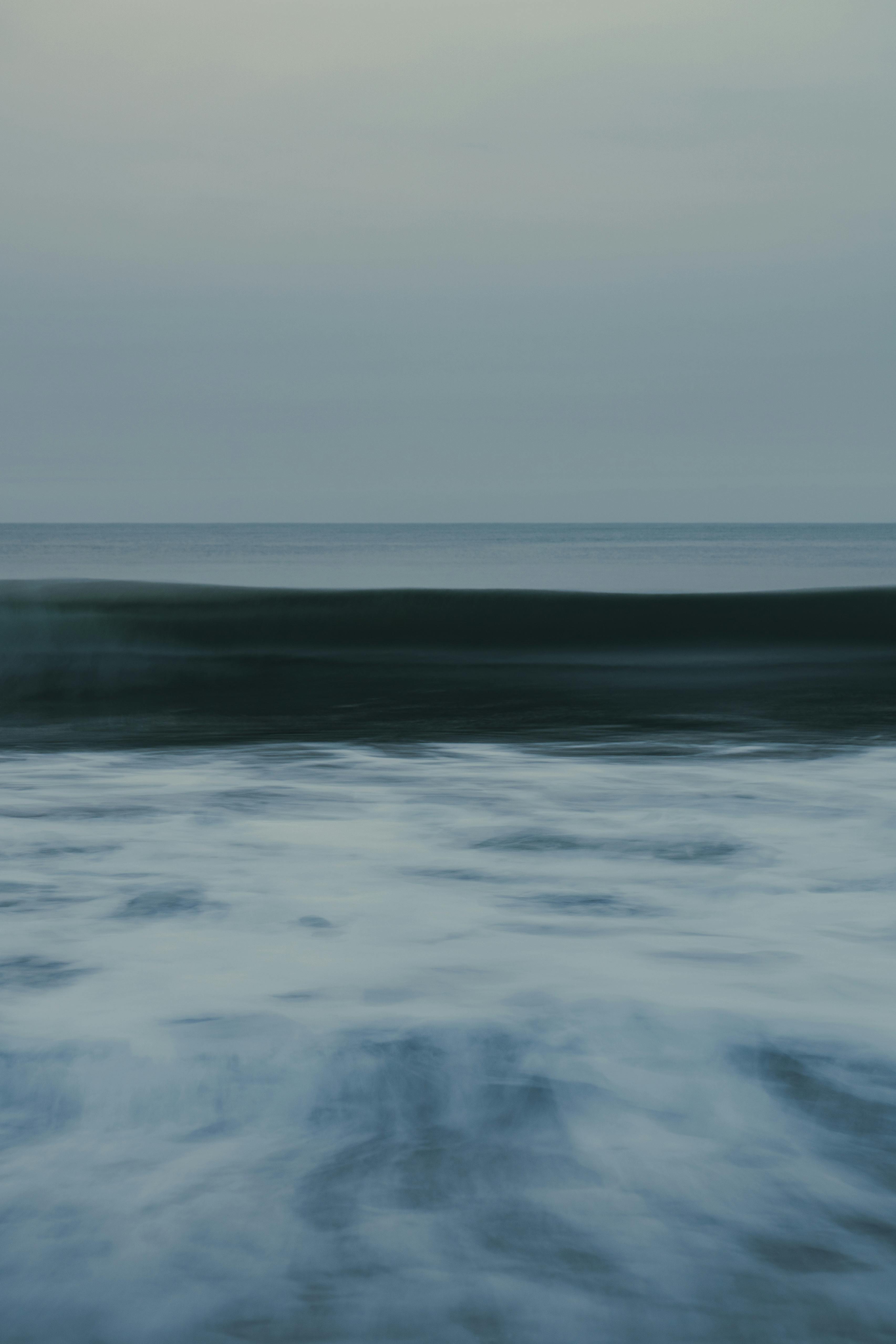 A tranquil view of ocean waves gently rolling under a pastel dusk sky.