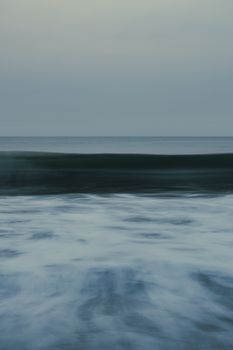 A tranquil view of ocean waves gently rolling under a pastel dusk sky.
