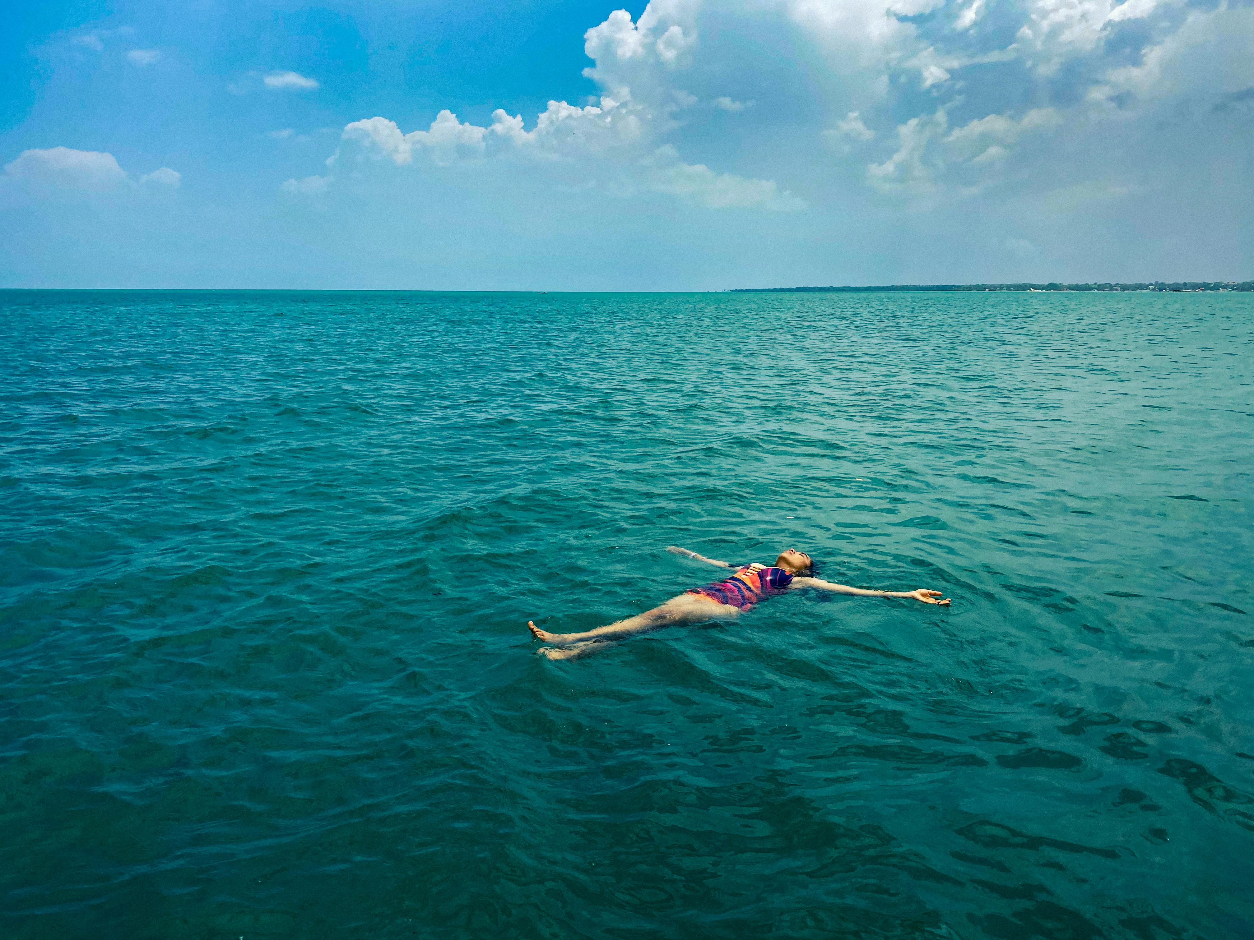 A woman in a swimsuit floats serenely in the ocean under a bright summer sky.