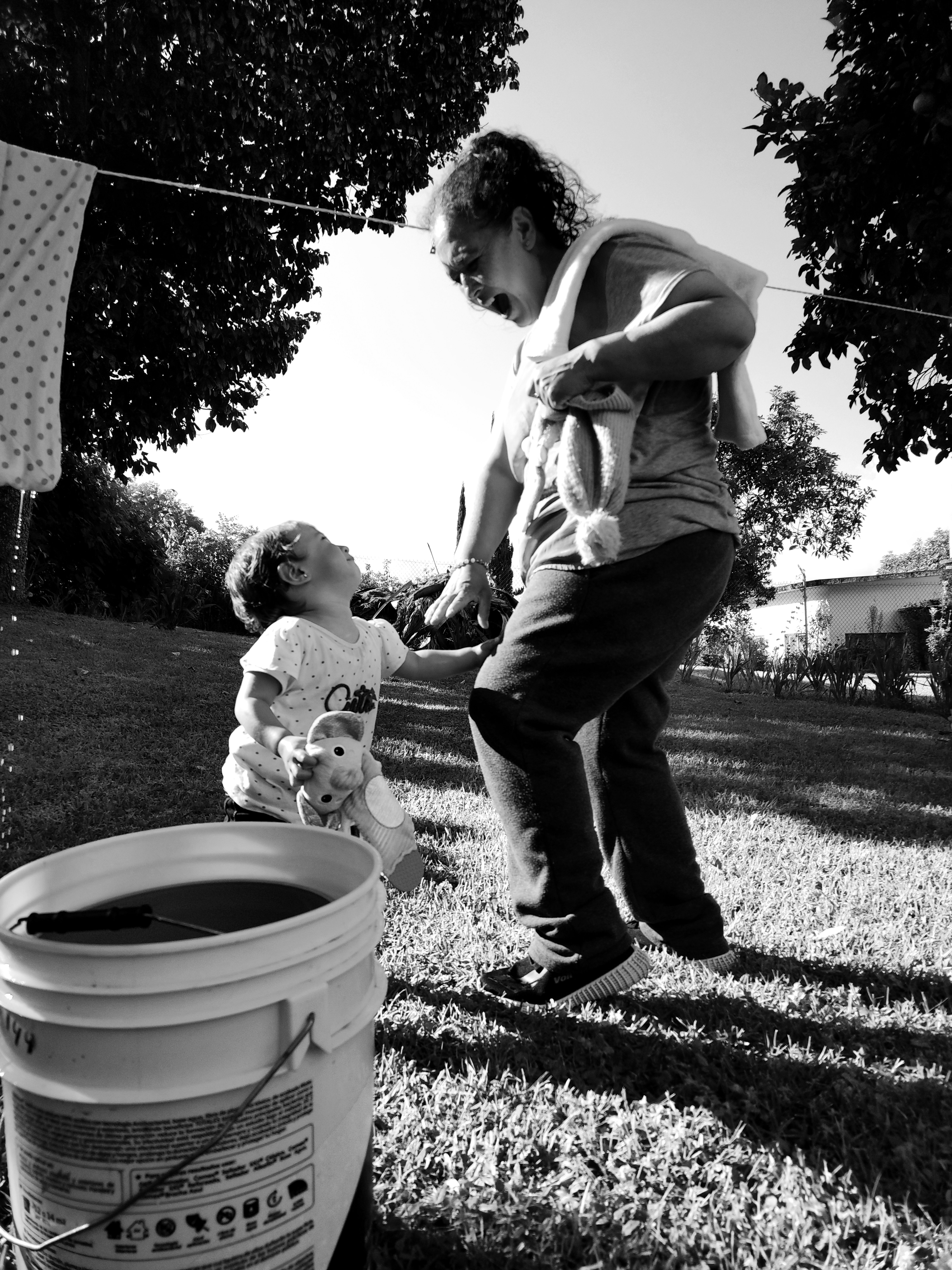 Black and white photo of a mother playing with her baby in a sunny garden.