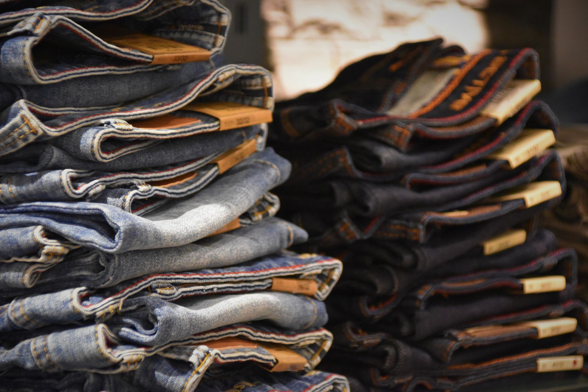 Stacks of folded denim jeans in several washes on a store shelf