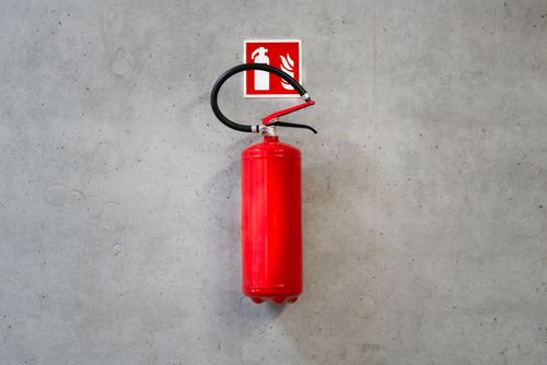 Free A red fire extinguisher mounted on a concrete wall indoors with emergency signage. Stock Photo