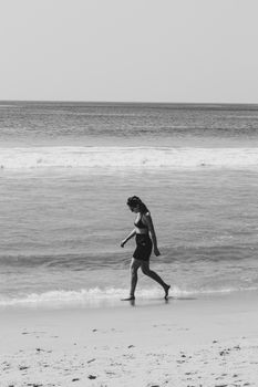 A woman enjoys a tranquil walk by the beach in Varkala, Kerala, India, captured in black and white.