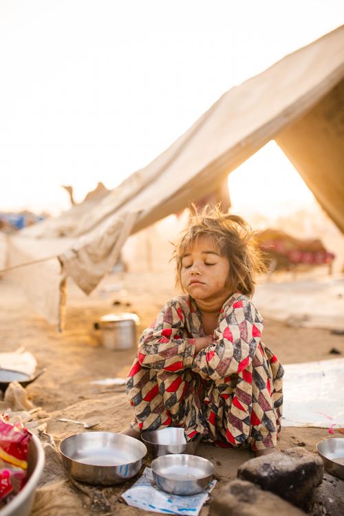 Free A young girl sits by metallic bowls in a sunlit desert camp in Pushkar, India. Stock Photo