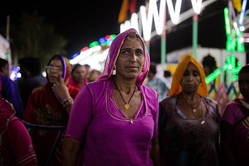 Women in pink saris stand in a crowd at night