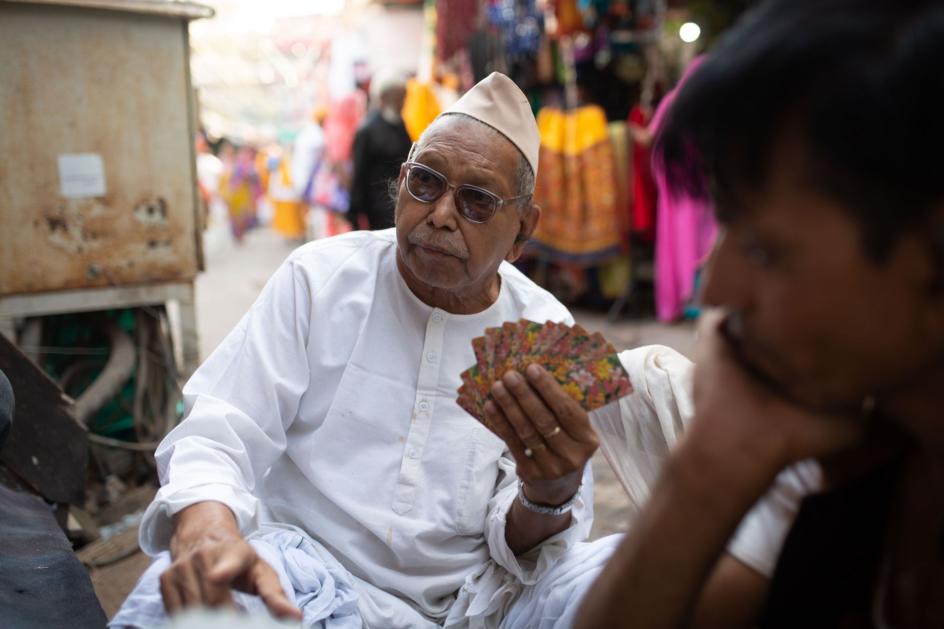 Elderly man in traditional attire playing cards in a vibrant Pushkar market.