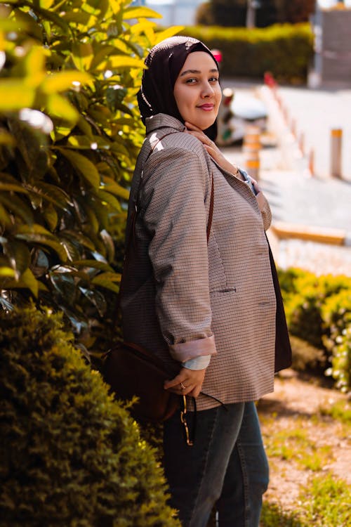 A woman in a hijab is standing in front of bushes