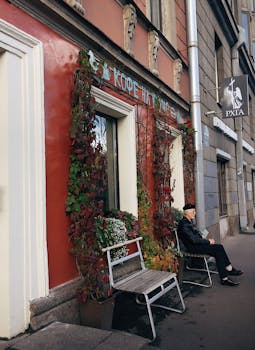 一位老人在圣彼得堡一家古色古香的咖啡店外放松身心，周围环绕着充满活力的常春藤