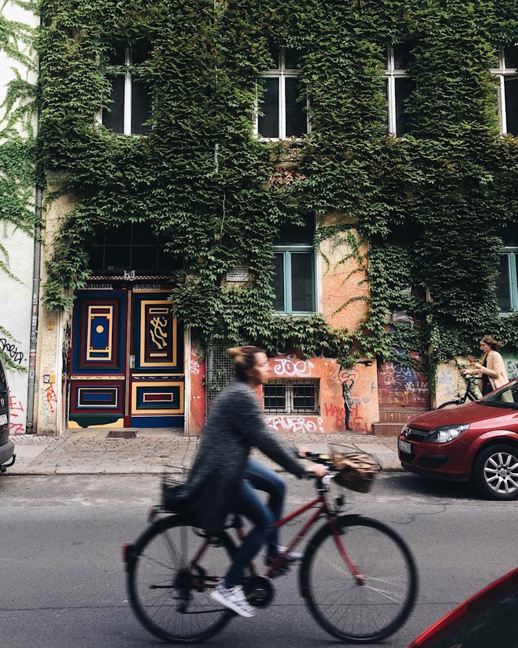 Person Riding On Bicycle Beside Concrete House With Green Vines