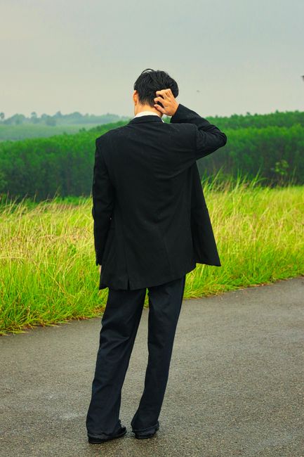Fotomural Un hombre con traje está de pie en un camino rural, ajustándose el cabello, con campos verdes al fondo.
